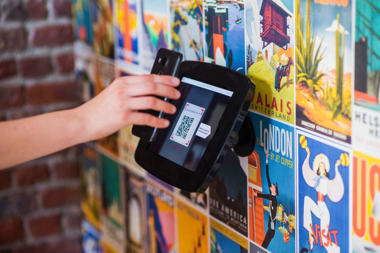 Home A hand scanning a QR code with a smartphone on a wall covered in vibrant posters indoors.