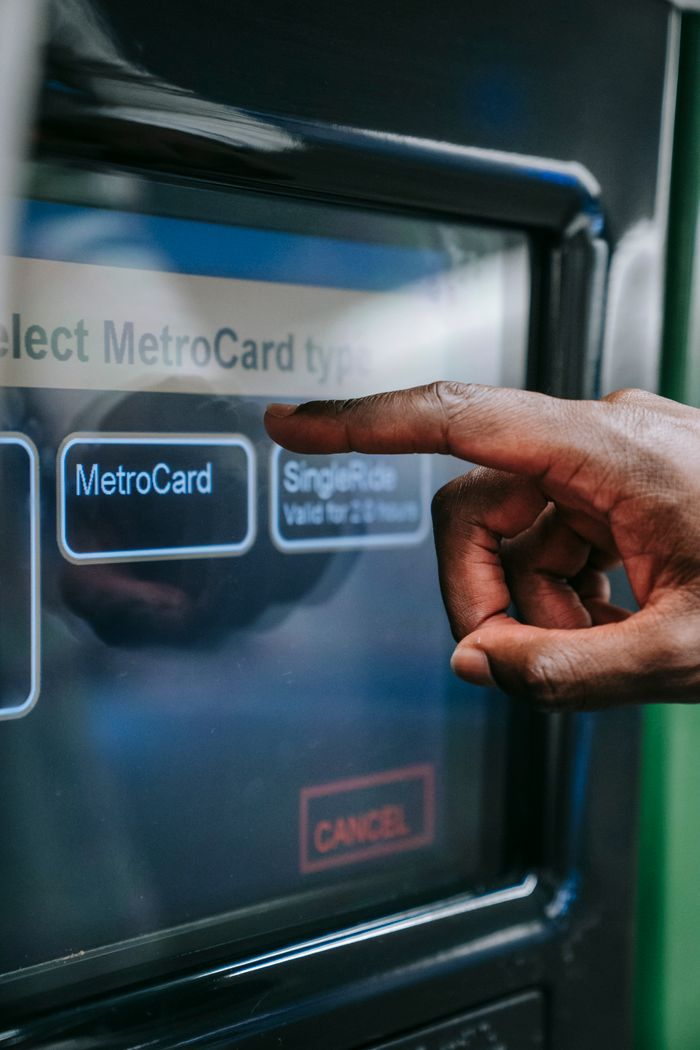 Home Close-up of a hand using a MetroCard payment touchscreen for subway access.